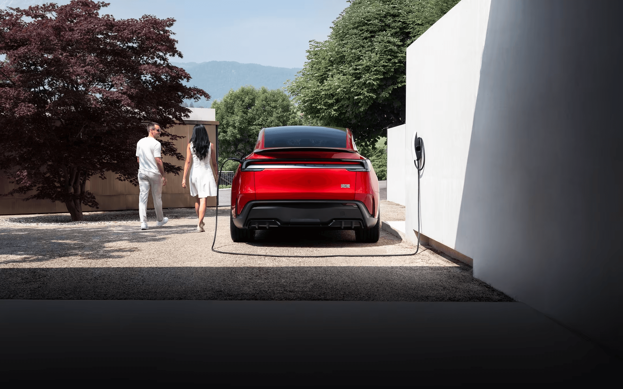 Red electric vehicle connected to a Tesla Wall Connector at a modern home